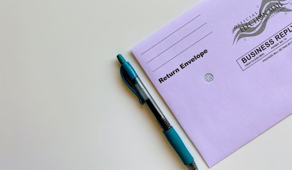 A purple absentee ballot envelop with a pen next to it